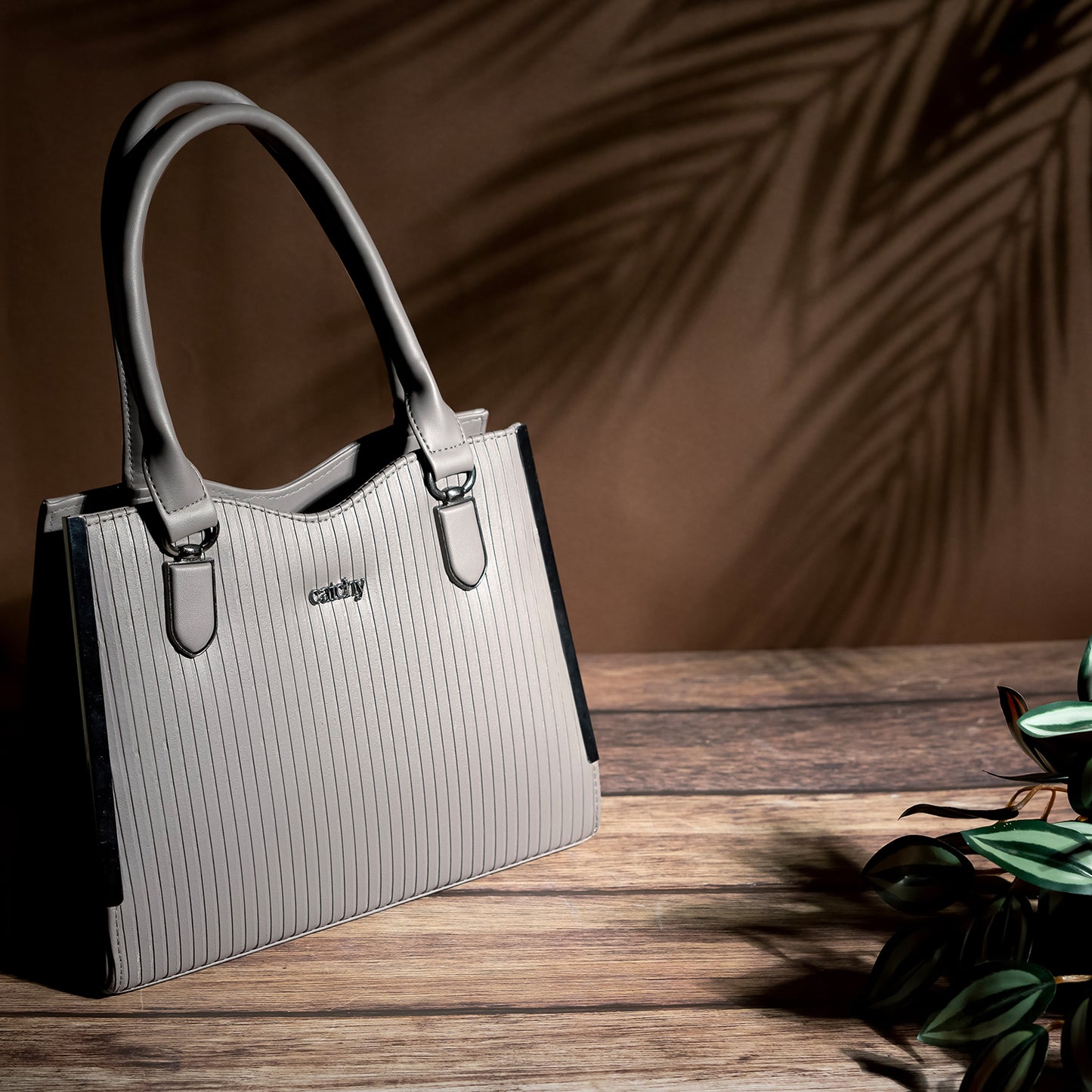 Elegant grey designer handbag with black accents, lightweight and stylish for everyday use, displayed on a wooden table.