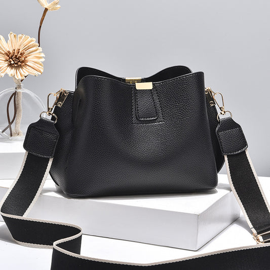 A black leather shoulder sling bag with a gold clasp and detachable black-and-white striped straps, set against a white background.