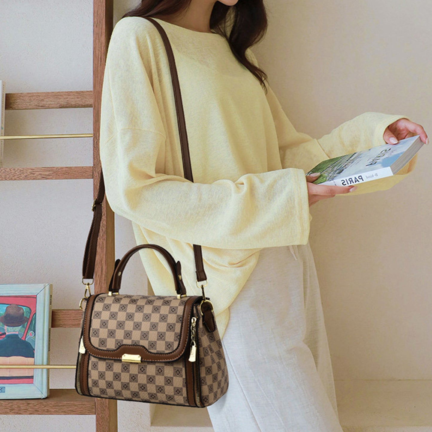A woman wearing a yellow sweater carrying a tan brown PU leather structured sling bag with a stylish handle and gold hardware, showcasing a comfortable and practical design.