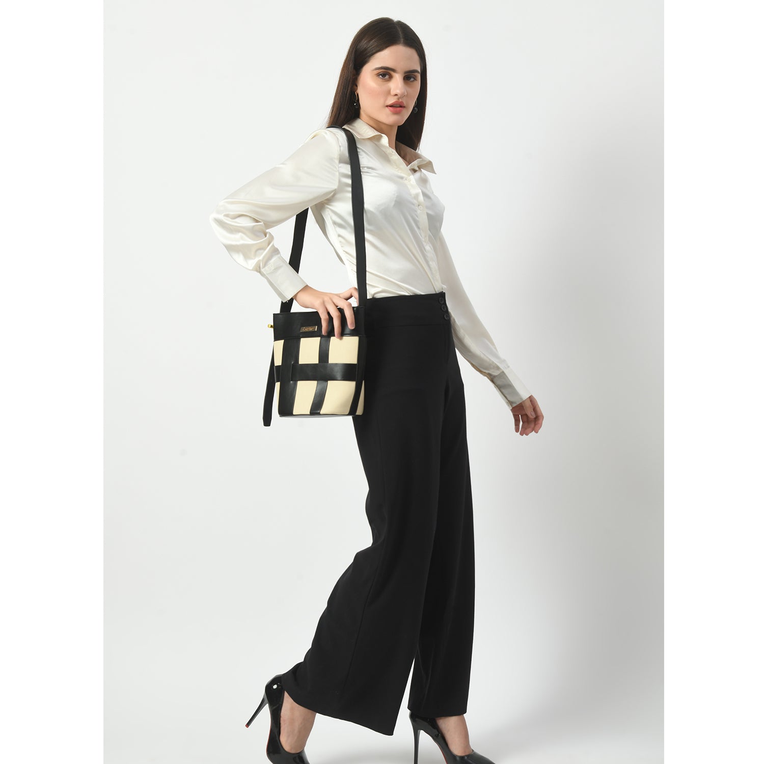 Woman showcasing stylish cream and black plaid canvas tote bag with black shoulder strap, complemented by cream blouse, black pants, and black high heels